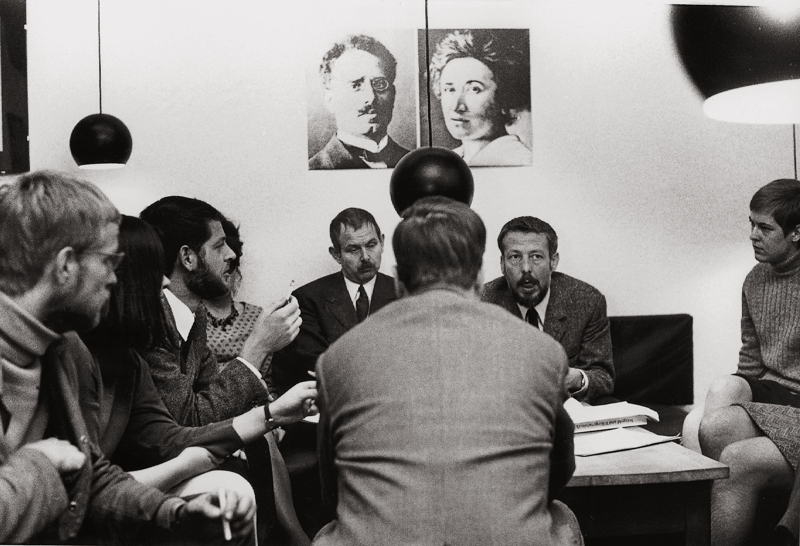 Sitzung im Republikanischen Club Köln unter den Portraits von Rosa Luxemburg und Karl Liebknecht. Auf dem Foto sind vier Frauen auszumachen.